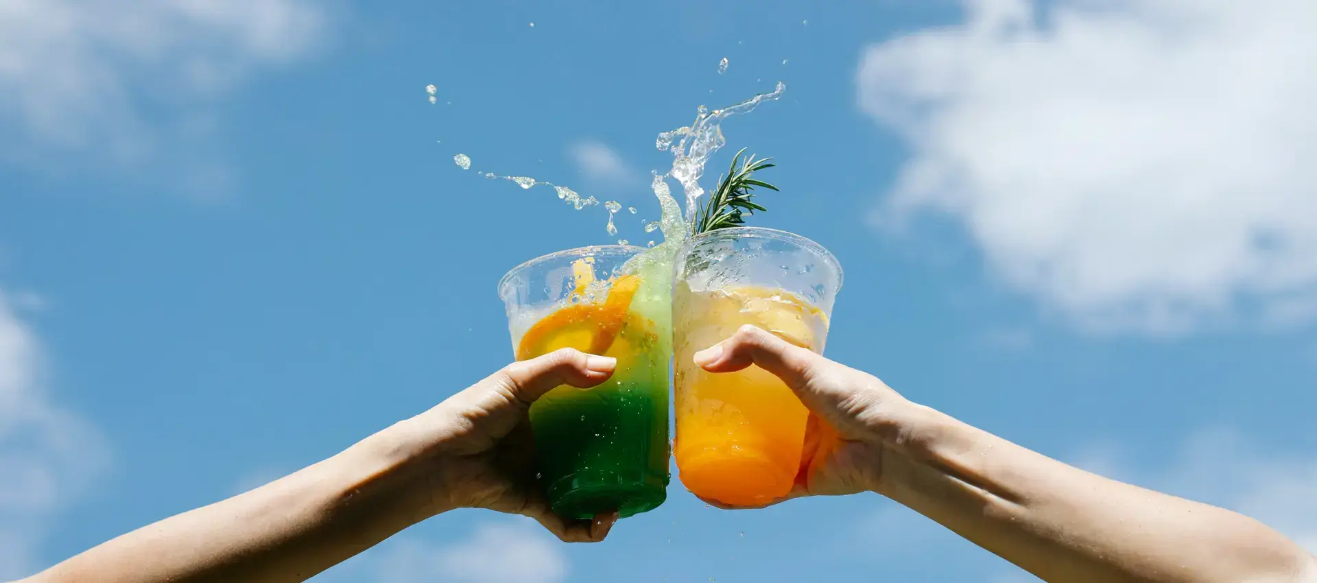 Friends toasting colorful summer drinks under a blue sky