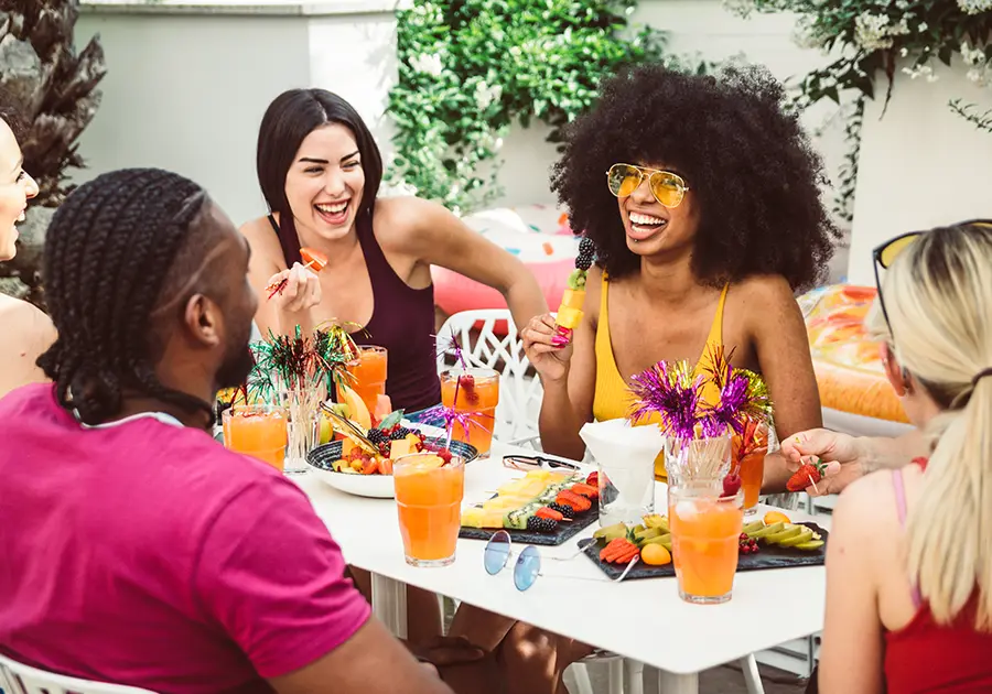 http://Group%20of%20people%20sitting%20outdoors%20around%20a%20table%20enjoying%20colorful%20drinks%20and%20fruit%20platters.